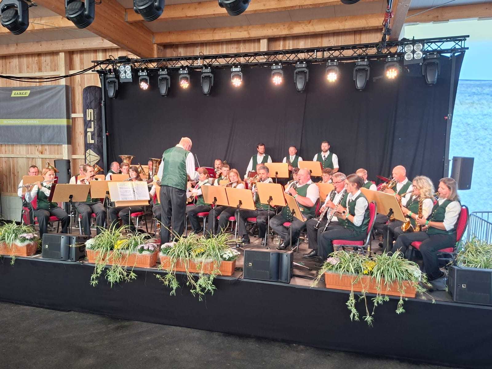 Musikkapelle mit Dirigent spielt auf einer Bühne in Österreich mit Blas- und Holzblasinstrumenten.
